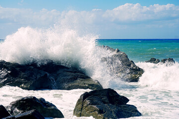 Beautiful shot of powerful waves crashing on big wet rocks at the beach