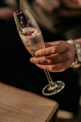 Happy Valentines day celebration concept. Man pouring sparkling champagne in glass with red heart shaped confetti. Love potion in glass. Close up