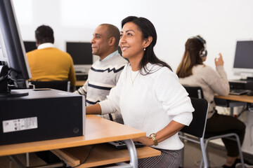 Smiling Latina engaged in self-education using pc for searching information in public library