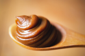 A spoonful of dulce de leche on a wooden spoon and brown backdrop. 