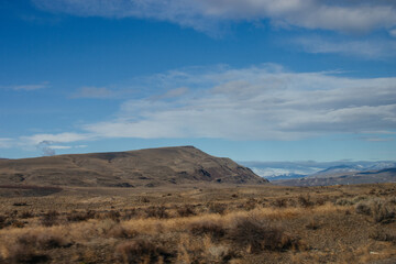 Beautiful autumn landscape with mountains on the horizon, blue sky with clouds and dry on the grass on the ground.