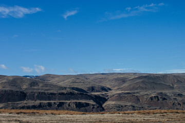 Beautiful autumn landscape with mountains on the horizon, blue sky with clouds and dry on the grass on the ground.