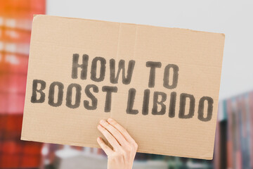 The phrase " How to boost libido " on a banner in men's hand with blurred background. Desire. Pleasure. Intimate. Intimacy. Relationship. Sex. Private life. Love. Bedroom. Sexual health