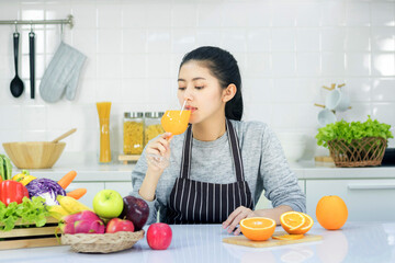 Asian women taking care of health and body shape Preparing food in the kitchen and waiting to drink orange juice in the glass.
