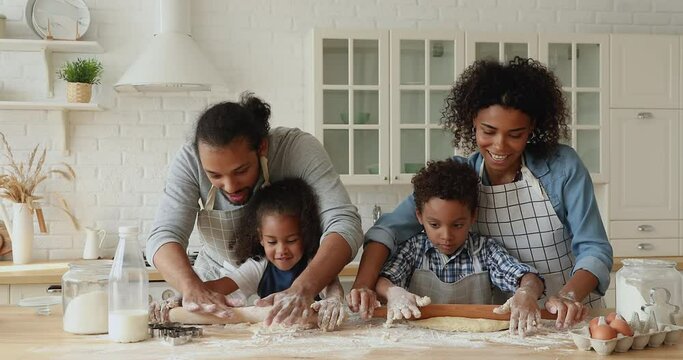 African couple with small 5s adorable kids preparing dough for cookies, happy family roll out dough with rolling pin enjoy process spend weekend together. Develop children, parenthood, cookery concept