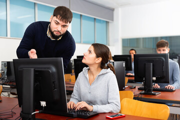 Glad cheerful male trainer helping young female student in computer class