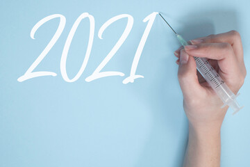HAND WRITING "2021" WITH A SYRINGE ON BLUE BACKGROUND