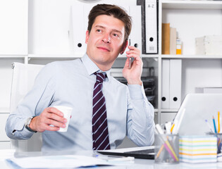 Young and smiling male office worker deciding and talking on the phone