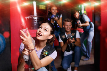 Portrait of young positive cheerful glad girl took aim colored laser guns during laser tag game in labyrinth