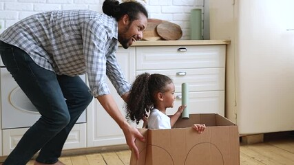 Slow motion African father riding little adorable 4s daughter while she sitting inside of cardboard box, active family play games at modern warm kitchen, celebrate relocation day to new home concept