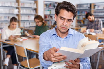 Portrait of focused intelligent man browsing books while visiting public library..