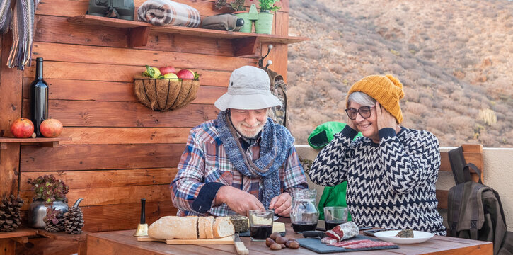 Senior couple of people having a snack with food and drink after a mountain hike. Two cheerful and smiling retired enjoying freedom and outdoors