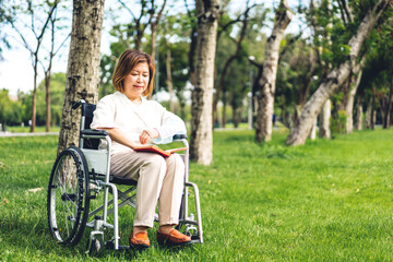 Fototapeta premium Senior adult elderly asia women sit on wheelchair and reading book outdoor