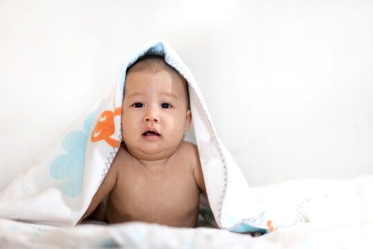 Portrait of happy smile baby boy relaxing looking at camera under towel after bath. Cute newborn child on the bed at home