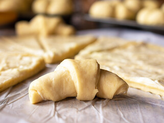 Close up of crescent roll.  Raised yeast dough has been rolled out for crescent rolls.  Dough has been lathered in butter.   Additional rolls in background.