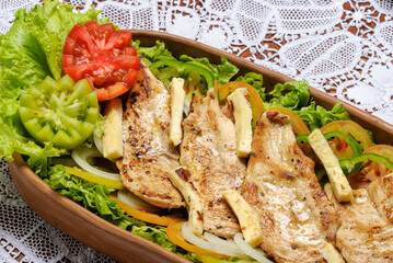 Sliced ​​chicken breast, grilled with rennet cheese and green salad served in clay bowl. Traditional Brazilian cuisine.