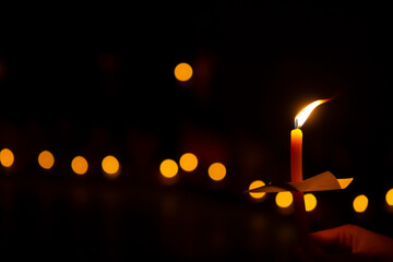 hand holding a burning candle in darkness with noise and grain effect bokeh.