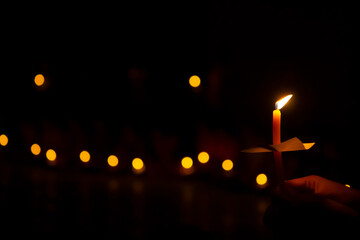 hand holding a burning candle in darkness with noise and grain effect bokeh.