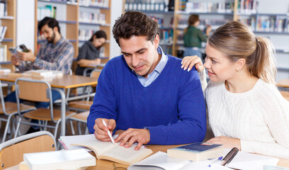 Portrait of couple of adult students studying together in public library ..