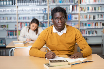 Portrait of adult african american student studying in university library, making notes in workbook