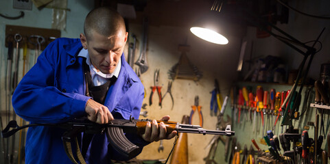 Concentrated skilled craftsman of weapons workshop disassembling AK assault rifle for repair .