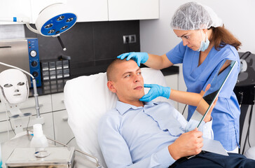 Obraz premium Female beautician examining face skin of young adult man before procedure at cosmetology clinic