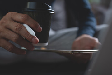 Close up of man hand holding digital tablet and cup of coffee during working from home
