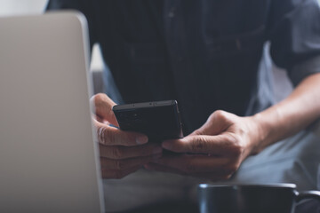 Man using mobile phone working on laptop computer in coffee shop