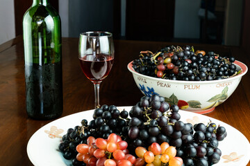 Freshly harvested red grapes and black grapes in ceramic plate with red wine in a glass.