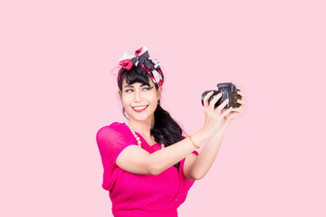 Like taking pictures. Closeup woman Holding camera pretty smiling pinup girl button shirt thinking about love career money looking hopeful to side, retro vintage 50's hairstyle isolated on color pink 