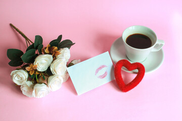 Cup of coffee with rose, kiss on white envelope and heart shape isolated on pink background