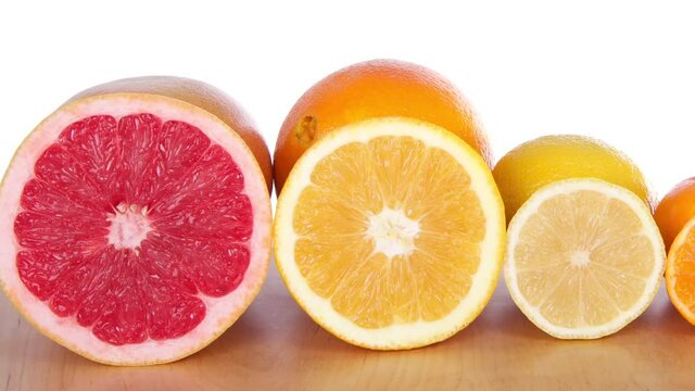 HD video panning across colorful sliced citrus lined up in rows on a light brown wood table with a white background. Grapefruit, naval orange, lemon, cuties clementine, lime and a key lime

