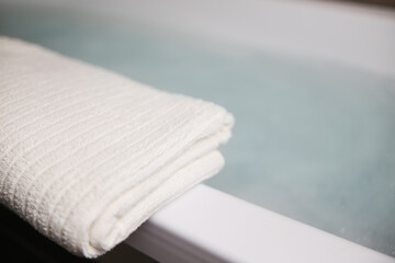 Fototapeta na wymiar A white towel on the edge of the tub. Blurred background gray blue colors
