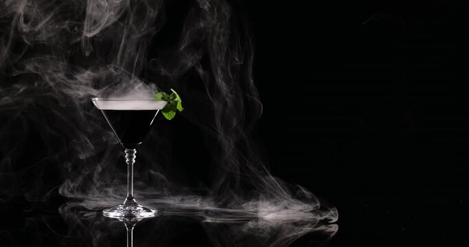 Glass of martini and smoke on black background
