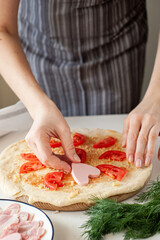 The process of making homemade pizza for Valentine's Day. Women's hands lay the ingredients cut in the form of hearts on the base of the dough.