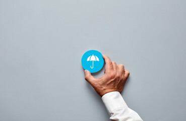 Businessman hand holding a blue badge with an umbrella icon representing insurance and protection.