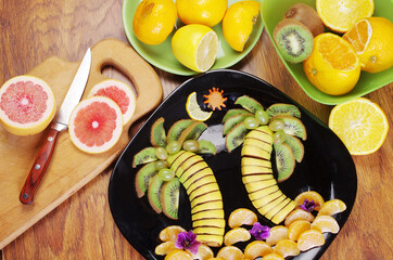 Fruit carving. Fruit dessert made from sliced bananas, kiwi, tangerines laid out on a plate in the shape of tropical palms. 