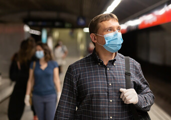 Fototapeta na wymiar Casual man wearing medical mask and rubber gloves waiting for train in platform of underground station. New life reality during COVID 19 pandemic..