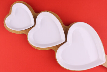 Set of white plates of different sizes in the shape of a heart on a wooden stand