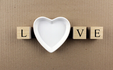 The inscription LOVE on wooden cubes and on a white plate in the shape of a heart on a cardboard background