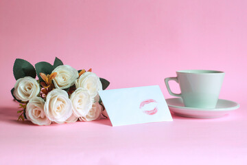 Cup of coffee with rose and kiss marked on white envelope isolated on pink background