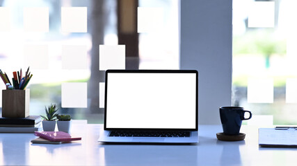 Mockup image of computer laptop, coffee cup, stationery and plant on white table. White empty screen for advertise text.