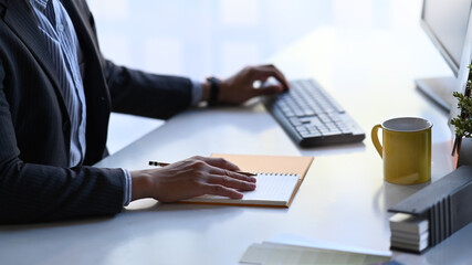 Close up view of businessman hands typing on keyboard and and writing something in her schedule...