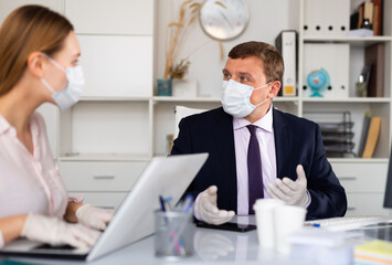 Director and secretary in protective medical masks work in the office