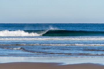 Wave breaking on a bright sunny morning. Perfect wave barrel with offshore wind on a sand beach break