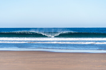 Fototapeta na wymiar Wave breaking on a bright sunny morning. Perfect wave barrel with offshore wind on a sand beach break