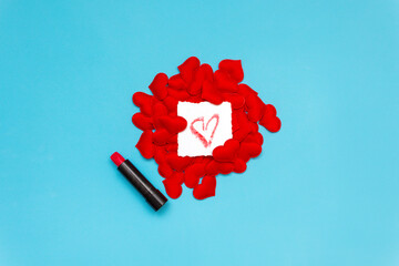 On the red hearts is a white square with a heart painted with lipstick, which lies next to it. Blue background. Minimal Valentine's Day greeting card with copy space. Border arrangement background