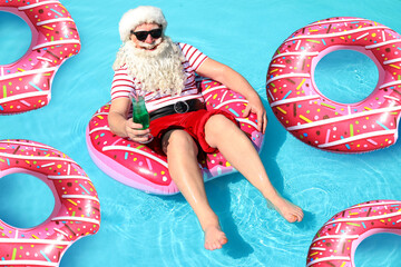 Santa Claus with inflatable rings relaxing in swimming pool