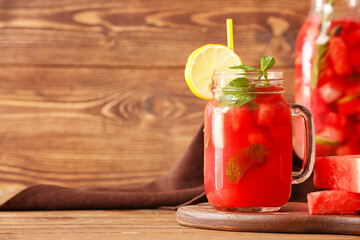 Mason jar and bottle of tasty cold watermelon lemonade on wooden table