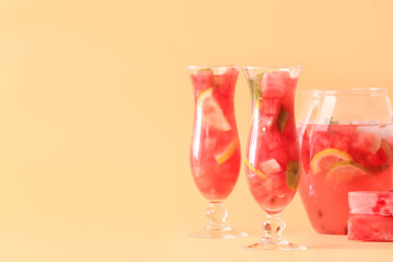 Jug and glasses of cold watermelon lemonade on color background